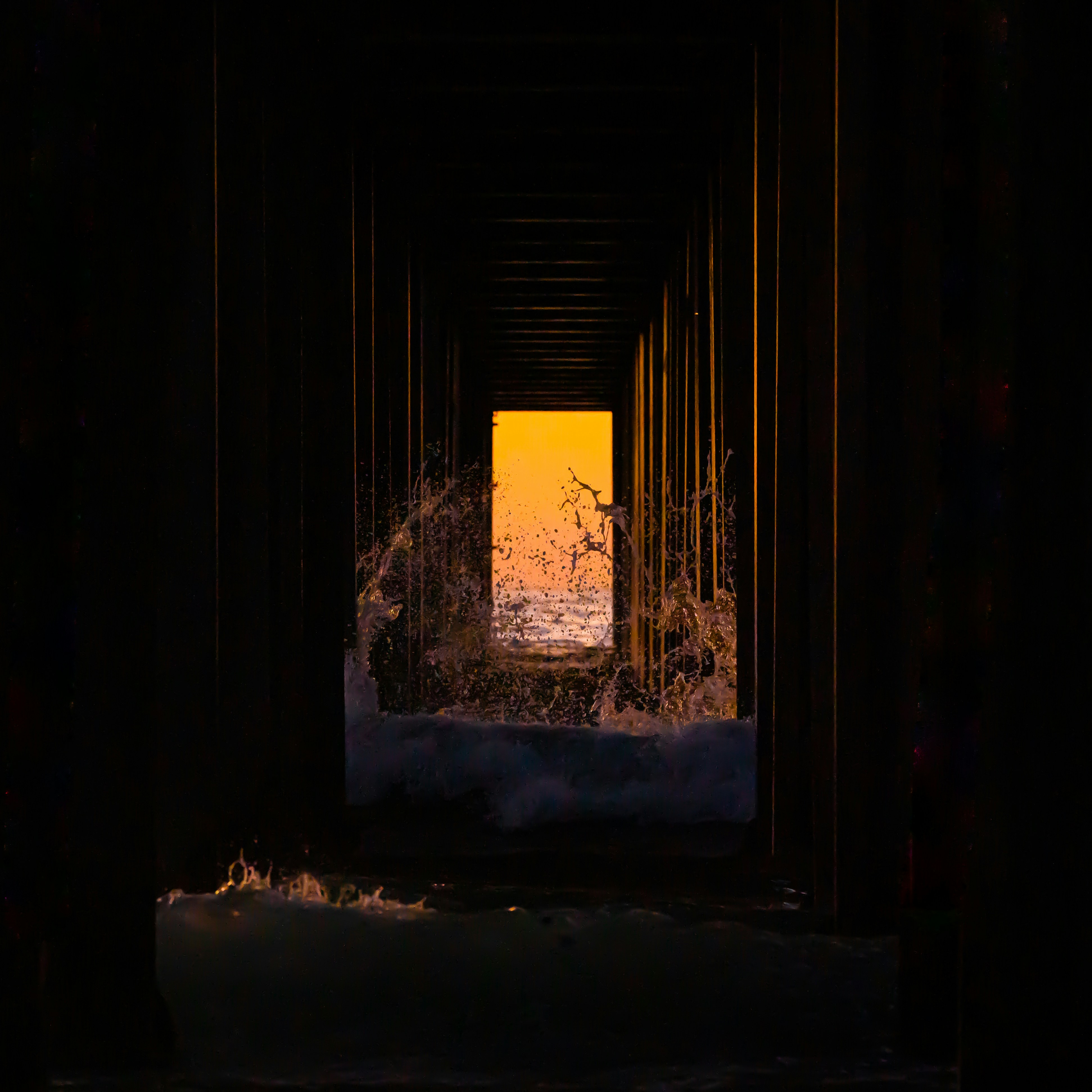 Ocean spray framed by a dark pier tunnel